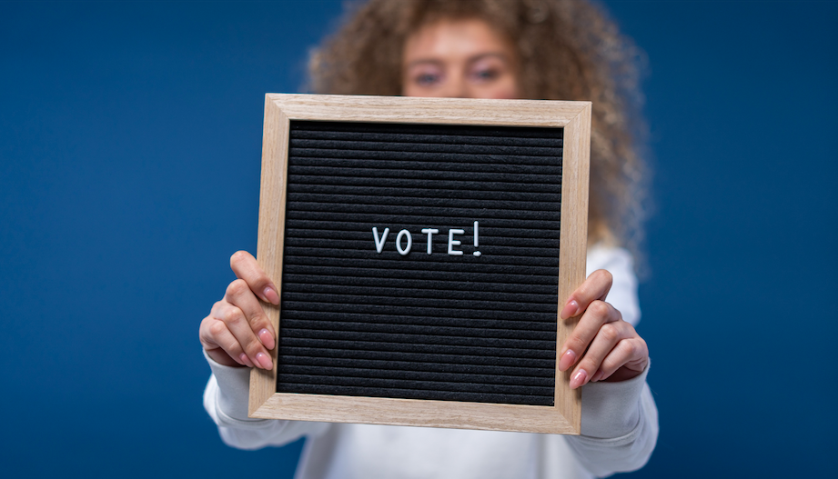 A blurred woman holds a sign that says VOTE.